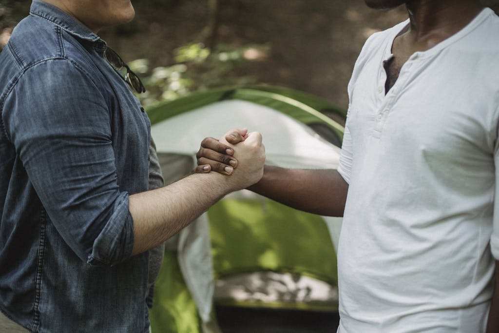 Male travelers shaking hands in campsite - The Explore Horizon